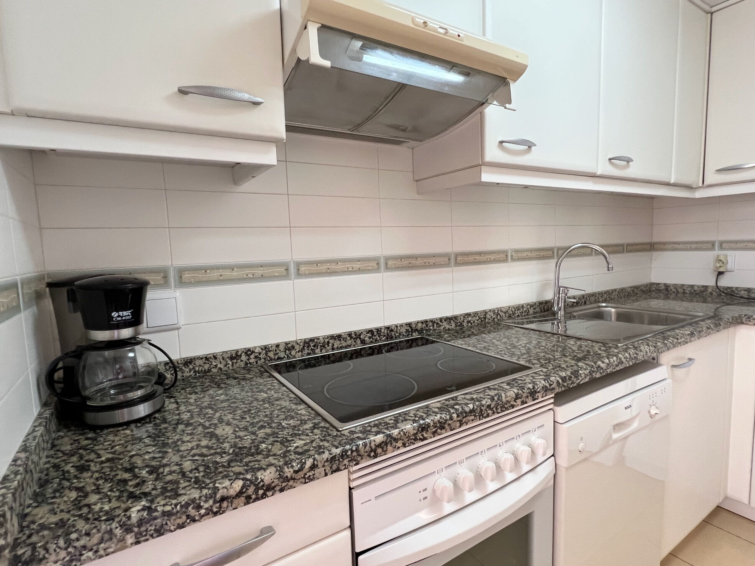 A kitchen with white cabinets, a granite countertop, a coffee maker, a sink, and a dishwasher.