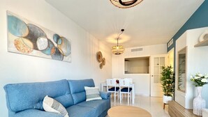 Una sala de estar moderna con un sofá azul, una mesa de centro de madera y un comedor con sillas blancas.