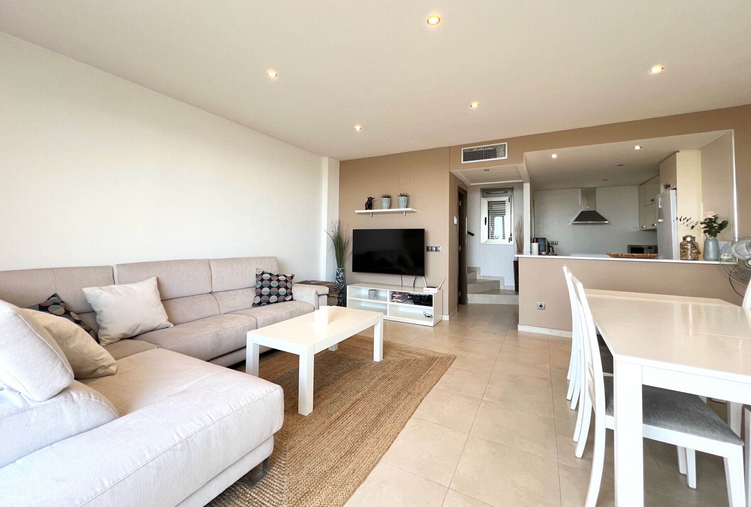 A modern living room with a sofa, coffee table, TV, and dining area.
