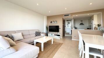 A modern living room with a sofa, coffee table, TV, and dining area.