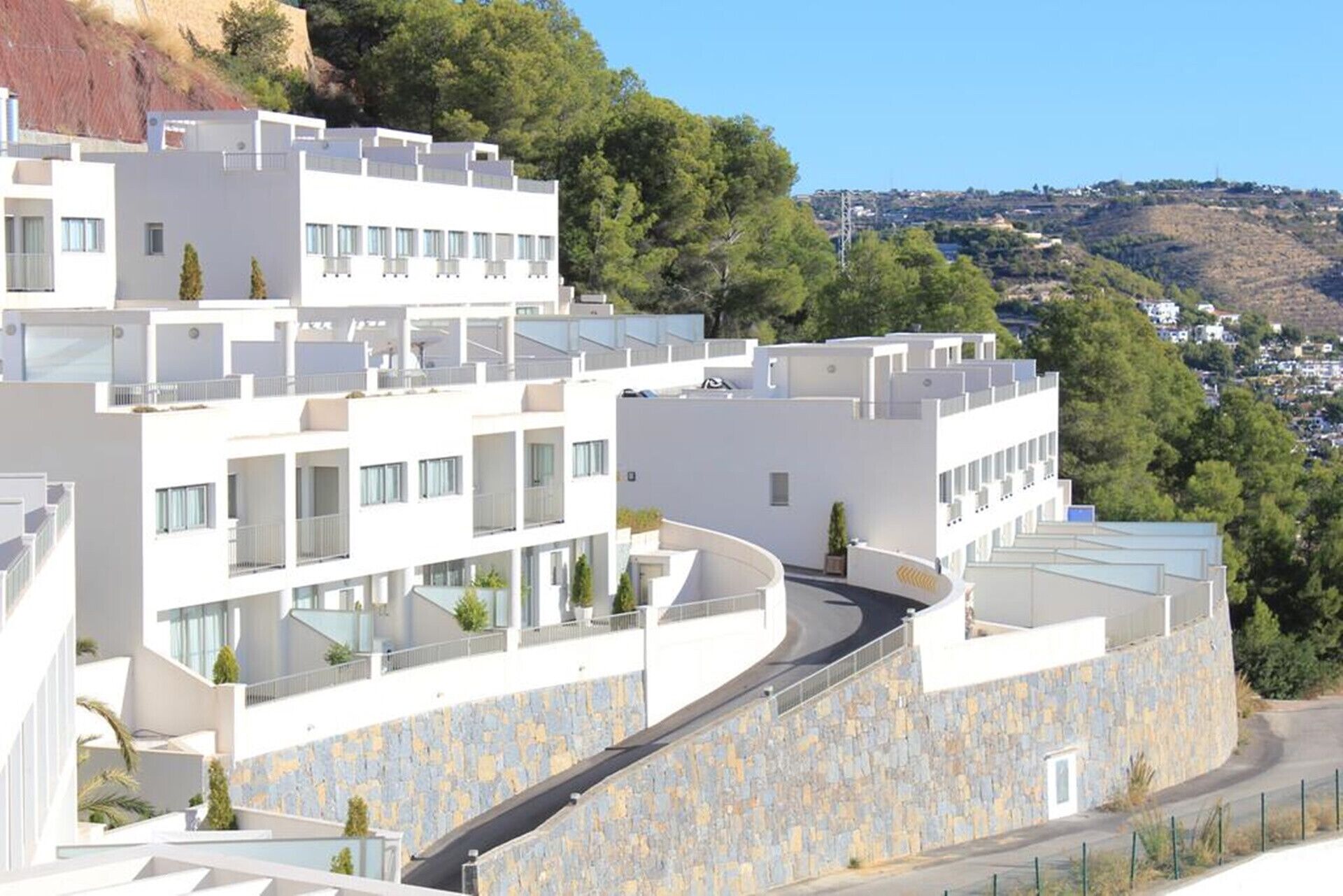 Un hotel moderno de varios pisos con un camino curvo y muros de piedra.