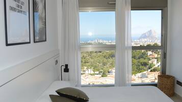 A hotel room with a large window offering a city view, a bed with pillows, and a wall-mounted power outlet.