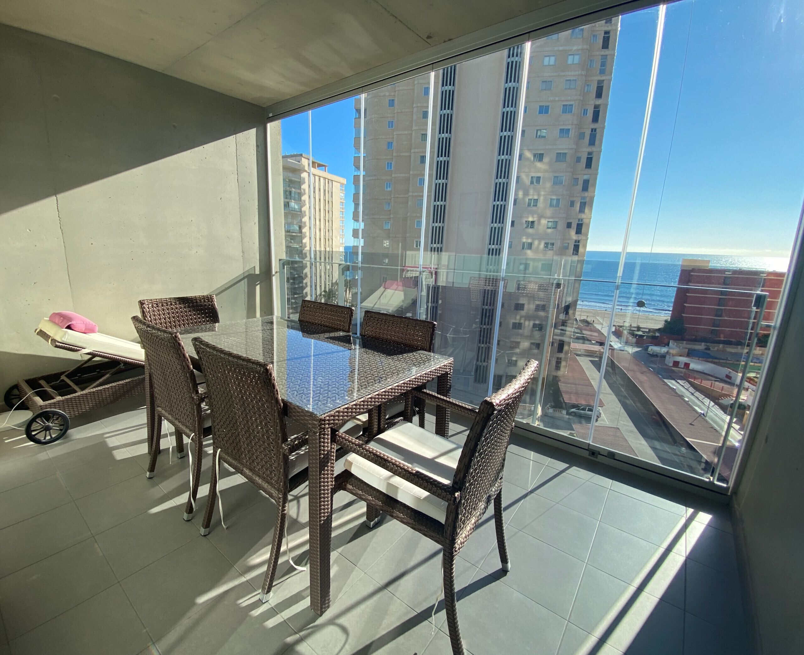Ein Balkon mit einem Glastisch und Korbstühlen, mit Blick auf eine Stadtlandschaft und den Ozean.