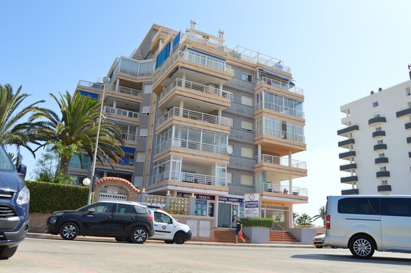 A multi-story hotel with balconies, a travel agency, and palm trees.
