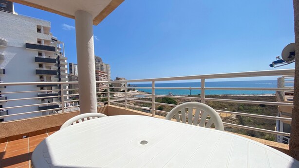 A balcony with a table and chairs, overlooking a coastal view with buildings and a clear sky. - Alq 156 Talima sea views (Calpe)