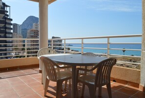 A balcony with a table and chairs, overlooking a coastal area with buildings and a mountain in the background. - Alq 156 Talima sea views (Calpe)