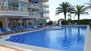 A swimming pool with blue water, surrounded by white lounge chairs, palm trees, and a building with balconies. - Alq 156 Talima sea views (Calpe)