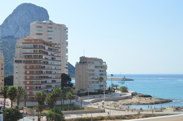 A coastal urban area with multi-story buildings, a beach promenade, and a rocky outcrop in the background.