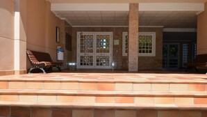 A covered outdoor area with steps leading to a door, benches, and a tiled floor.