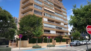 A multi-story residential building with balconies, a gated entrance, and a parking area.