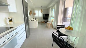 Et moderne køkken med hvide skabe, en indbygget ovn og et spiseområde med et bord og stole.