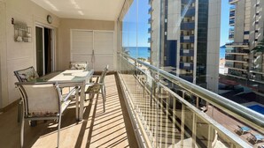 A balcony with a table and chairs, a view of the sea, and high-rise buildings in the background. - Alq 043 Porto Azul 4 (Calpe)