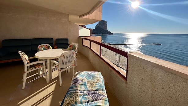 A balcony with a table and chairs, a sofa, and a view of the sea and a rock formation. - Alq 178 Amatista Apartment (Calpe / Calp)
