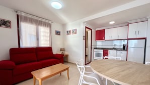A compact living space with a red sofa, a wooden table, white chairs, a kitchen area with red and white cabinets, and a small dining table. - Alq 178 Amatista Apartment (Calpe / Calp)