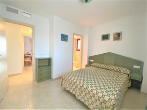 A bedroom with a bed, a dresser, a chair, and a door leading to a bathroom. - Alq 178 Amatista Apartment (Calpe / Calp)