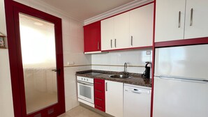 A kitchen with white and red cabinets, a stainless steel sink, a stove, and a dishwasher. - Alq 178 Amatista Apartment (Calpe / Calp)