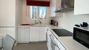 A modern kitchen with white cabinets, a red window valance, a built-in dishwasher, a black induction cooktop, and a stainless steel range hood.