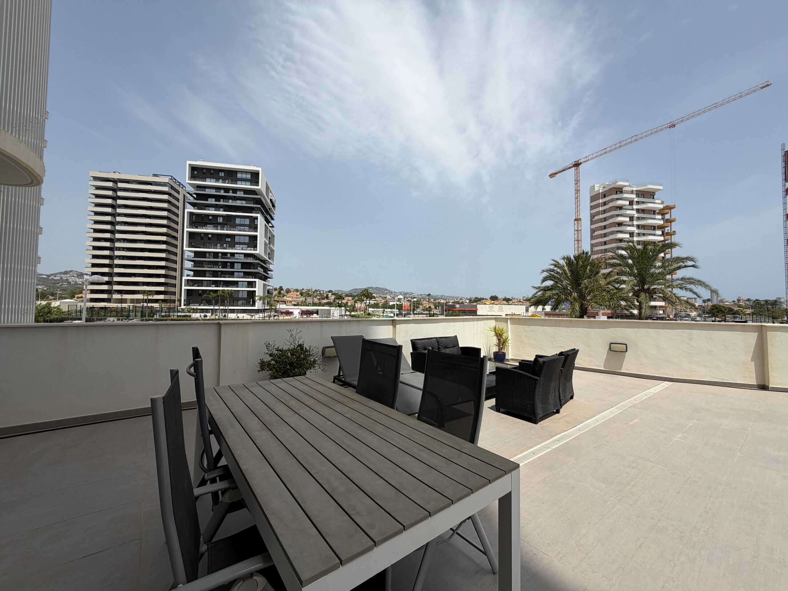Terraza en la azotea con una mesa y sillas, con vista a un paisaje urbano con edificios modernos y una grúa de construcción.