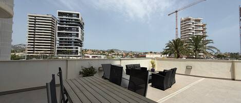 Terraza en la azotea con una mesa y sillas, con vista a un paisaje urbano con edificios modernos y una grúa de construcción.