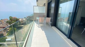 A balcony with a glass railing overlooking a coastal view, a table with chairs, and a large window. - Alq 229 Calpe Beach (Calpe / Calp)
