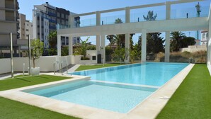 Piscina retangular com superfície de água azul translúcida, rodeada por um gramado verde bem cuidado e área de piscina em branco.