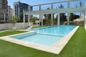 Une piscine rectangulaire à l’eau d’un bleu limpide, entourée d’une pelouse bien entretenue et bordée de dalles de béton blanc.