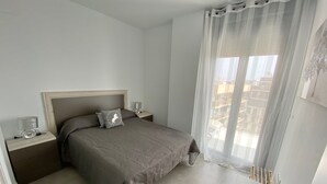 Quarto com cama, mesas de cabeceira, abajur, janela com cortinas e vista para edifícios.