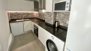 Uma cozinha compacta com máquina de lavar louça, forno, micro-ondas e chaleira sobre o balcão.