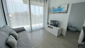 Uma sala de estar com um sofá cinzento, uma televisão sobre um armário branco e um quadro de uma bicicleta na parede.