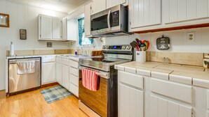 Una cocina con armarios blancos, horno de acero inoxidable, microondas y encimera de madera.