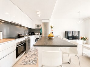 Ett modernt kök med vita skåp, en köksö, en mikrovågsugn, en kaffebryggare och en tvättmaskin.