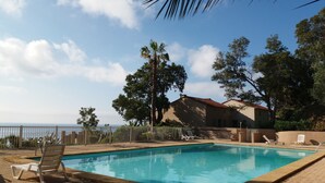 Una piscina rectangular con borde de azulejos, rodeada por un patio de ladrillo. Se observan sillas de descanso y una cerca.