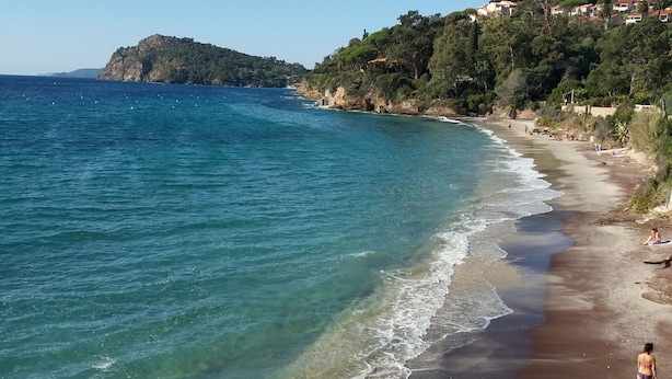 Una playa con aguas cristalinas, costa rocosa y un paisaje montañoso con edificios.