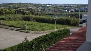 A balcony with red tiles overlooking a green landscape and a town in the distance.