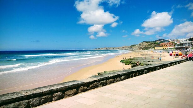 A beach with a stone wall and buildings in the background.
