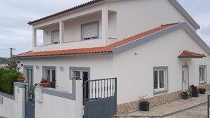 A two-story house with a tiled roof, a balcony with potted plants, and a gated entrance.