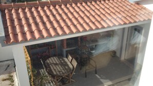 A glass-enclosed balcony with a tiled roof, a dining table, chairs, and potted plants.