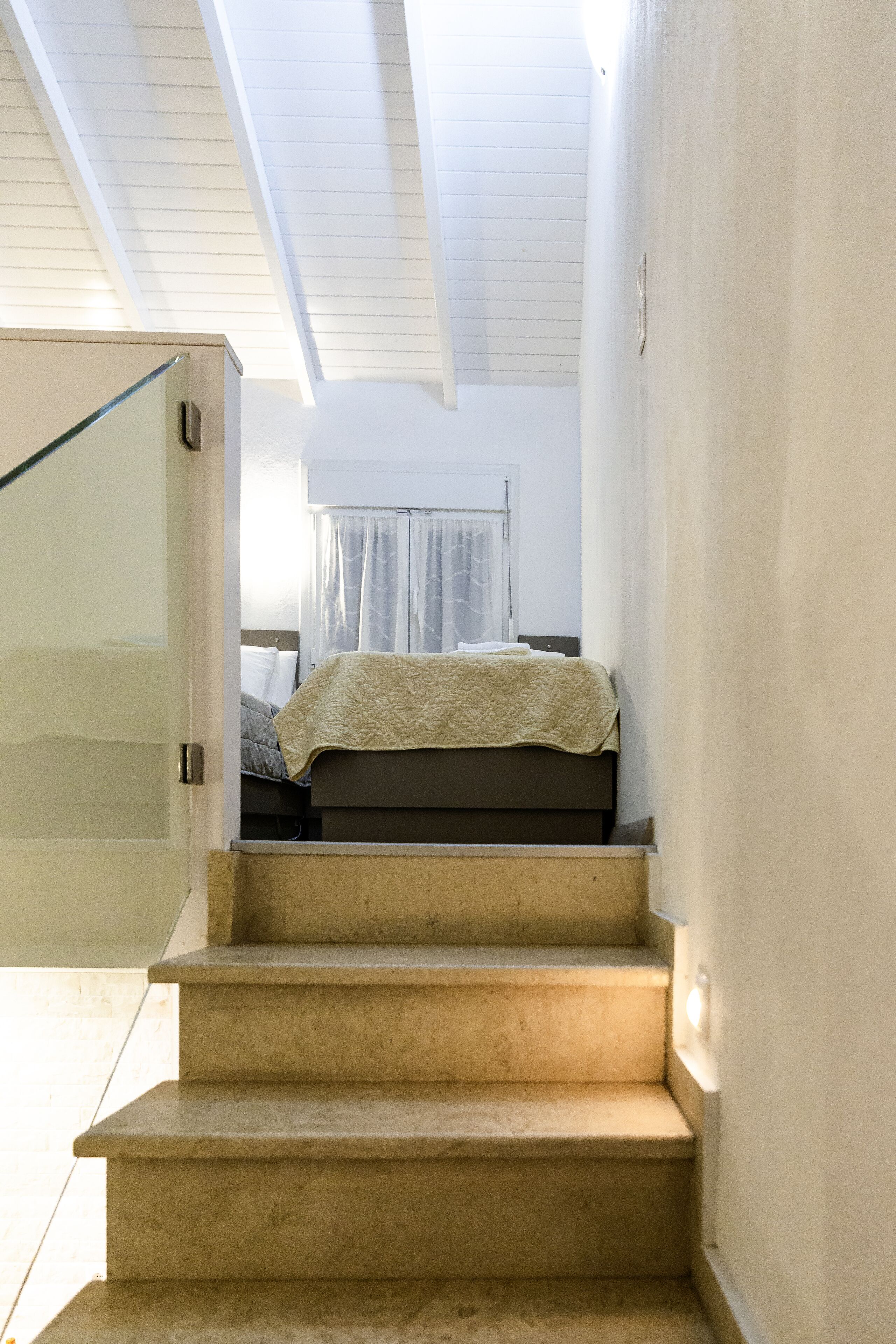 A staircase leading to a bedroom with a bed, a window with curtains, and a white ceiling.