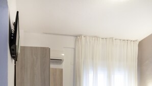 Un dormitorio moderno con cama, televisor de pantalla plana montado en la pared y mesita de noche con lámpara.
