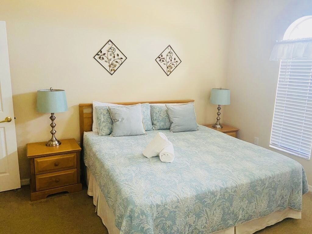 A bedroom with a bed, two nightstands, two lamps, and two wall art pieces.