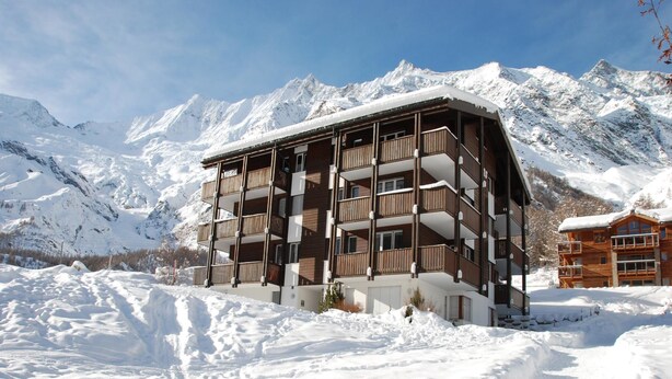 A multi-story wooden building with balconies, surrounded by snow-covered mountains. - Topas 24 by Interhome (Saas-Fee)