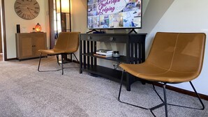 Un salon moderne doté d’un grand téléviseur à écran plat affichant un montage d’images, de deux fauteuils en cuir, d’un meuble en bois et d’une horloge murale.