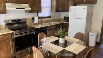 A modern kitchen with wooden cabinets, stainless steel appliances, a glass dining table, and a potted plant.