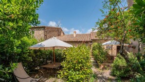 A rustic outdoor patio with a stone wall, a table with a metal chair, and a large umbrella providing shade.