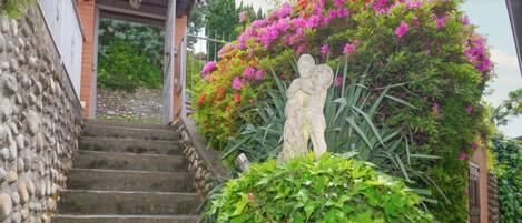 Un escalier en pierre mène à une pergola en bois ornée d’une statue représentant un enfant et une femme.