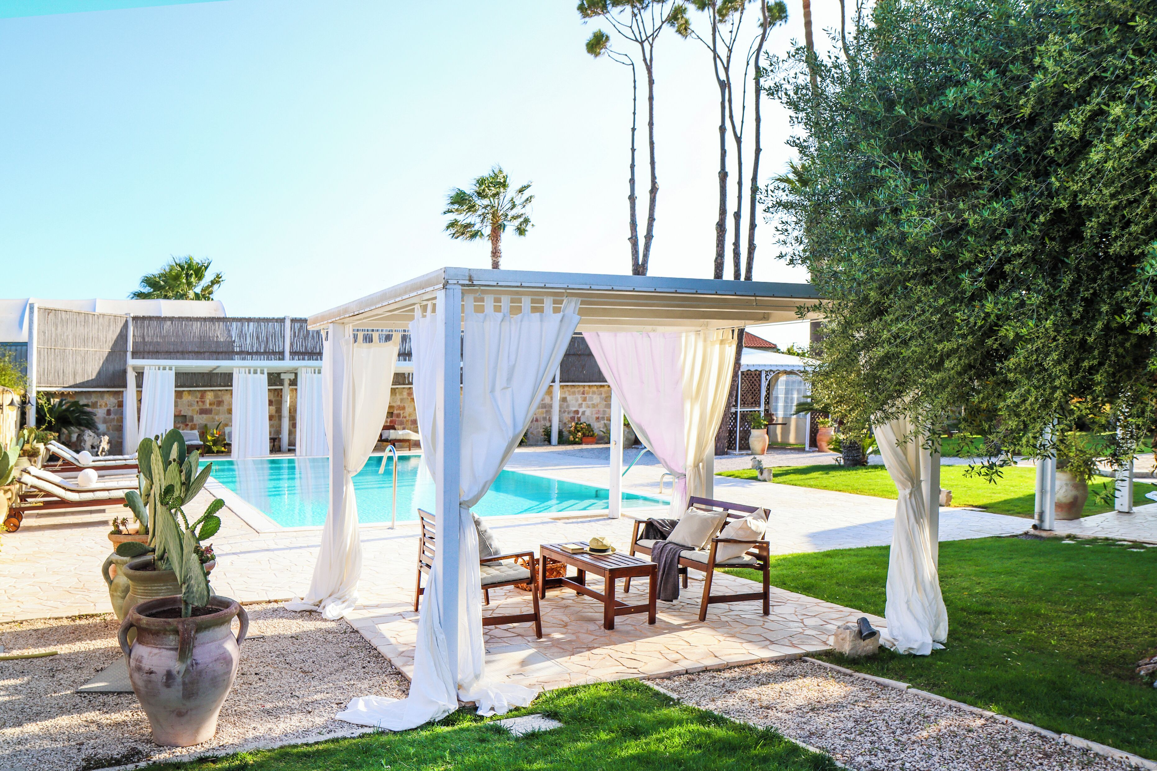 A poolside area with a covered seating area, a pool, and a well-maintained lawn.