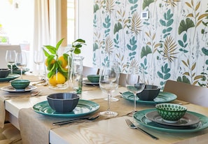 A dining table set with green plates, bowls, and wine glasses, with a vase of lemons and a plant on the table. - Villa Erika SicilyMyHome (Ispica)