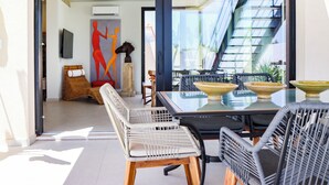 A modern dining area with wicker chairs, a glass table, and a view of a staircase and greenery outside.