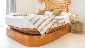 A bed with a woven headboard, white bedding, and a gold lamp beside it.