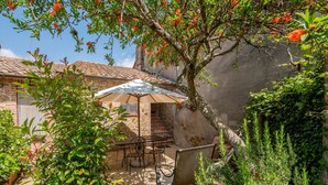 Un patio al aire libre con una mesa y sillas, rodeado de follaje y un muro de piedra.